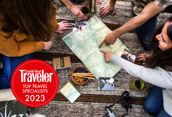 Knowmad team members working together to create an itinerary, pointing at a map, with a Condé Nast Traveler 2023 seal on the lower left.